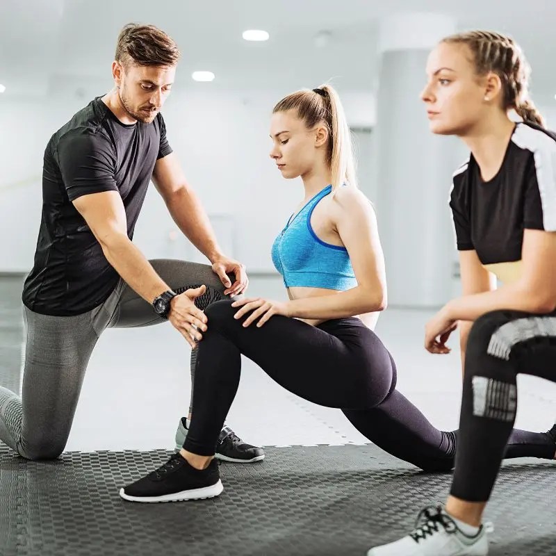A certified personal trainer demonstrates a deep leg stretch to a female client in Arlington Heights, IL.