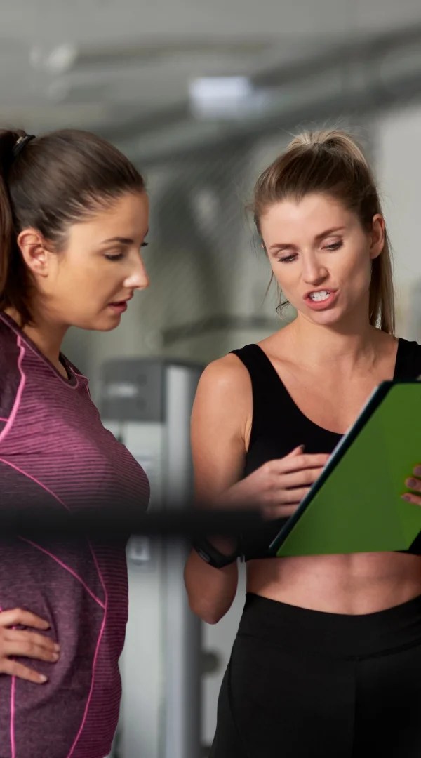 Female personal trainer reviewing customized fitness training services clipboard with a client in Palatine.