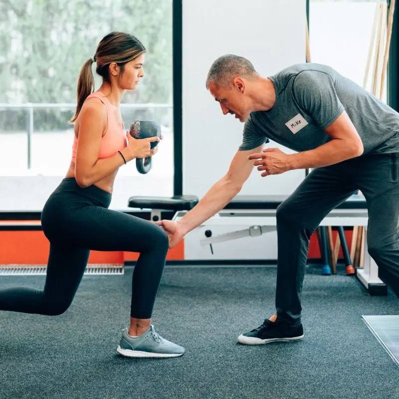 A professional fitness coach provides guided personalized workout support for a woman doing a lunge with a kettlebell in Palatine, IL.