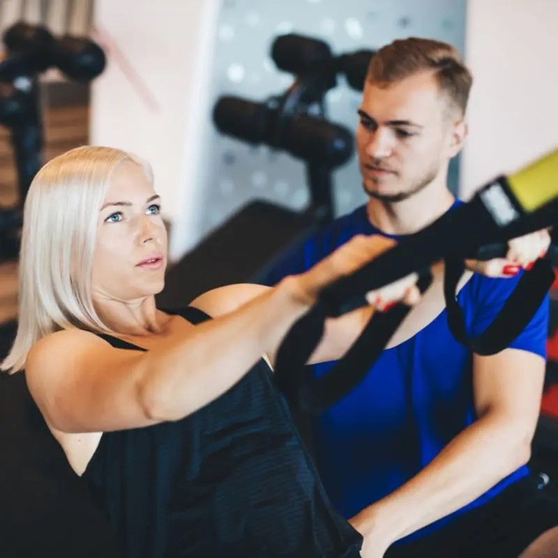 A blonde woman exercises using suspension training straps coached by a trainer in Palatine, IL.
