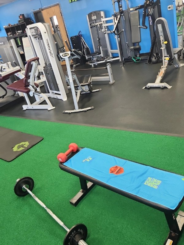Weight bench with barbell and red dumbbell on green turf floor in Arlington Heights.