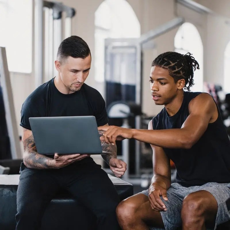 A personal trainer reviews personalized workout planning data on a laptop with a client in a fitness facility in Schaumburg, IL.